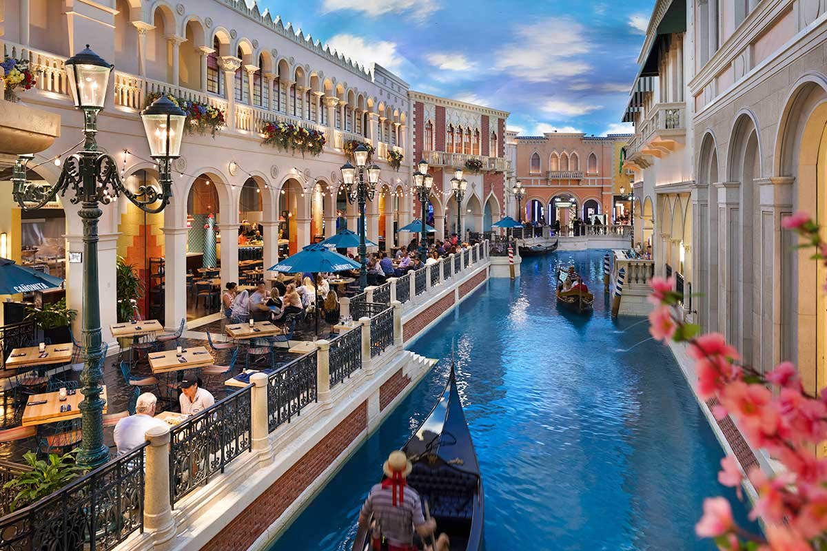 Guests dining in an al fresco style seating area beside gondolas gliding through water. 