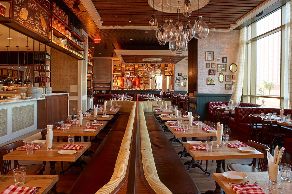 Cozy restaurant interior with wooden tables, checkered napkins, cushioned seating, and pendant lights hanging from the ceiling.