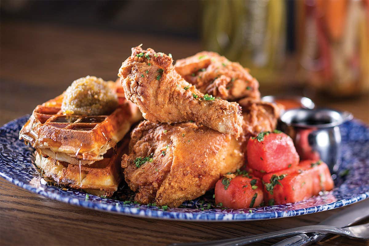 A plate of fried chicken, waffles with syrup, and garnished watermelon slices.